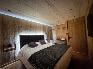 Un dormitorio con techo de madera, cama con cabecera negra y mesita de noche.