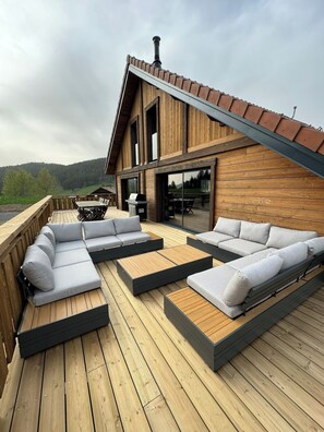 Eine Holzterrasse mit einer fest eingebauten Couch und einem Grill.