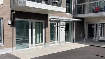 A modern building with a glass facade, a balcony with outdoor seating, and a visible entrance with a door marked "7C".
