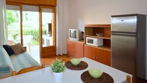 A compact kitchen with a refrigerator, microwave, and a television on a wooden cabinet. - Family house with garden and pool (Bibione)