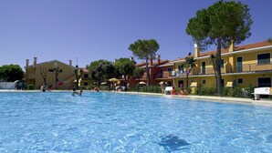 A swimming pool with people around it, surrounded by buildings with balconies and trees.