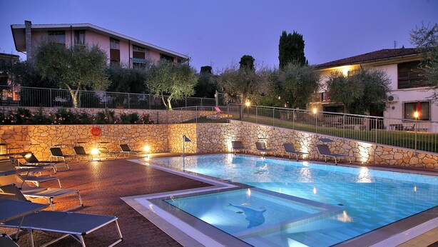 A swimming pool with lounge chairs and a stone wall. - Residence Uliveto (Garda)