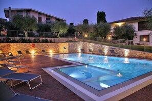 A swimming pool with lounge chairs and a stone wall. - Residence Uliveto (Garda)