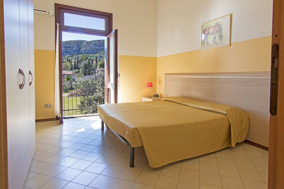 A bedroom with a bed, a nightstand, a lamp, and a window with a view of a mountain and trees.