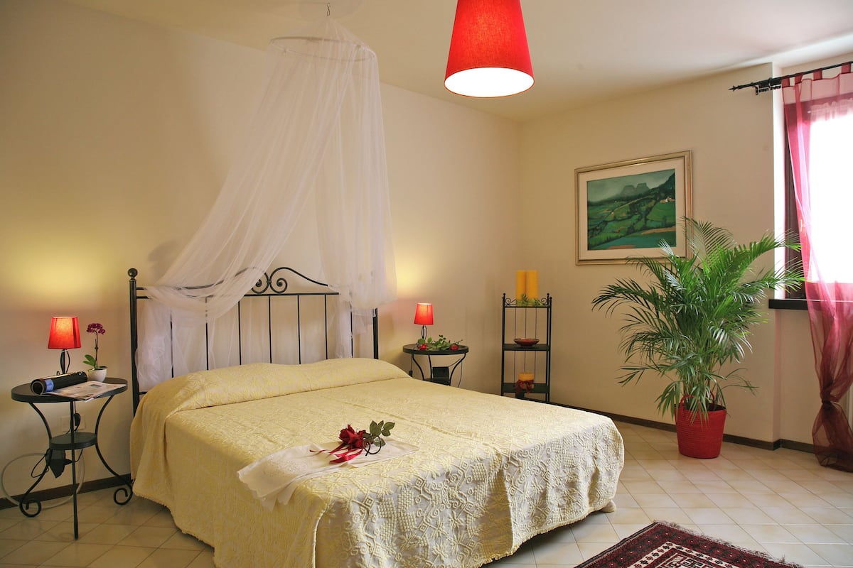 A neatly arranged bedroom with a bed, bedside tables, a bedside lamp, a potted plant, and a window with curtains.