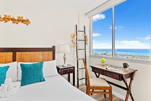 Una camera d'albergo con un letto, una scrivania, una sedia, una finestra vista oceano e un elemento decorativo a parete.