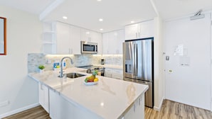 A modern kitchen with white cabinets, stainless steel appliances, and a marble countertop. - Ocean View 1BR at Ilikai Marina  (Honolulu)