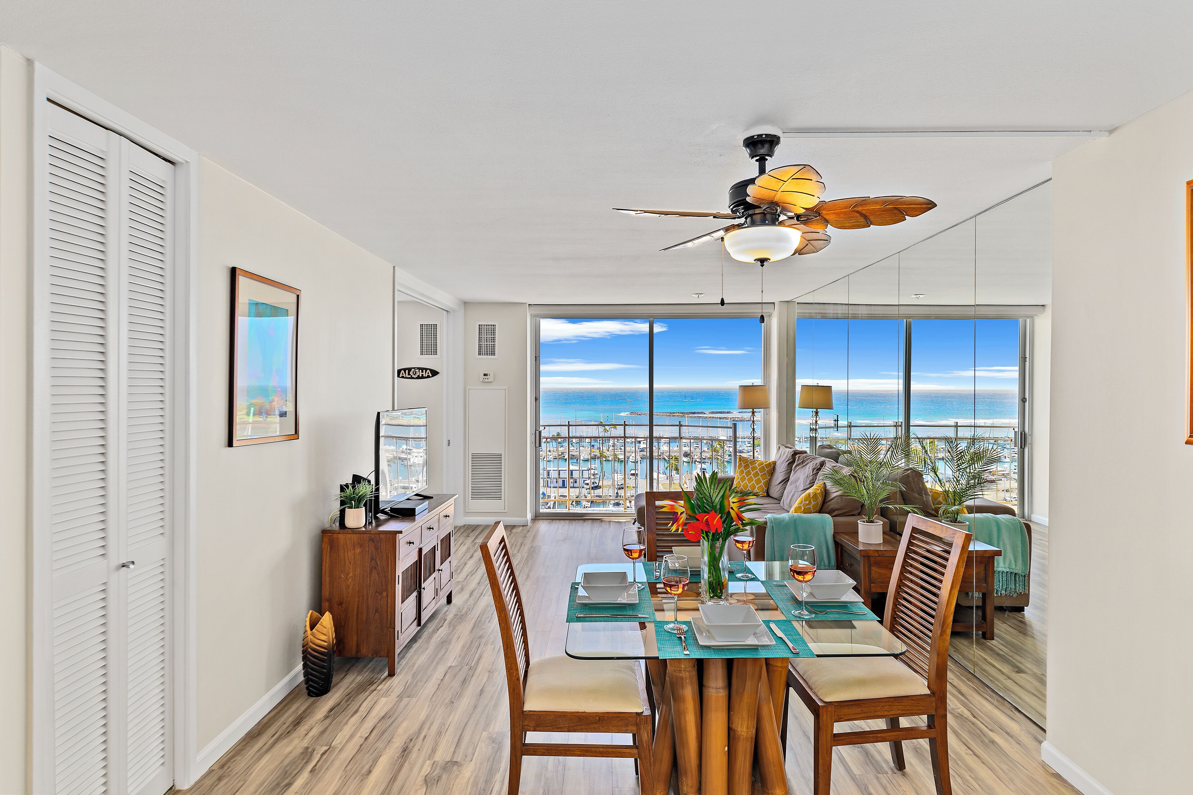 A dining area with a view of the beach, a ceiling fan, and a dining table set with plates and glasses.