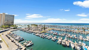 A marina with numerous boats docked, a clear blue sky, and a large building in the background. - Ocean View 1BR at Ilikai Marina  (Honolulu)