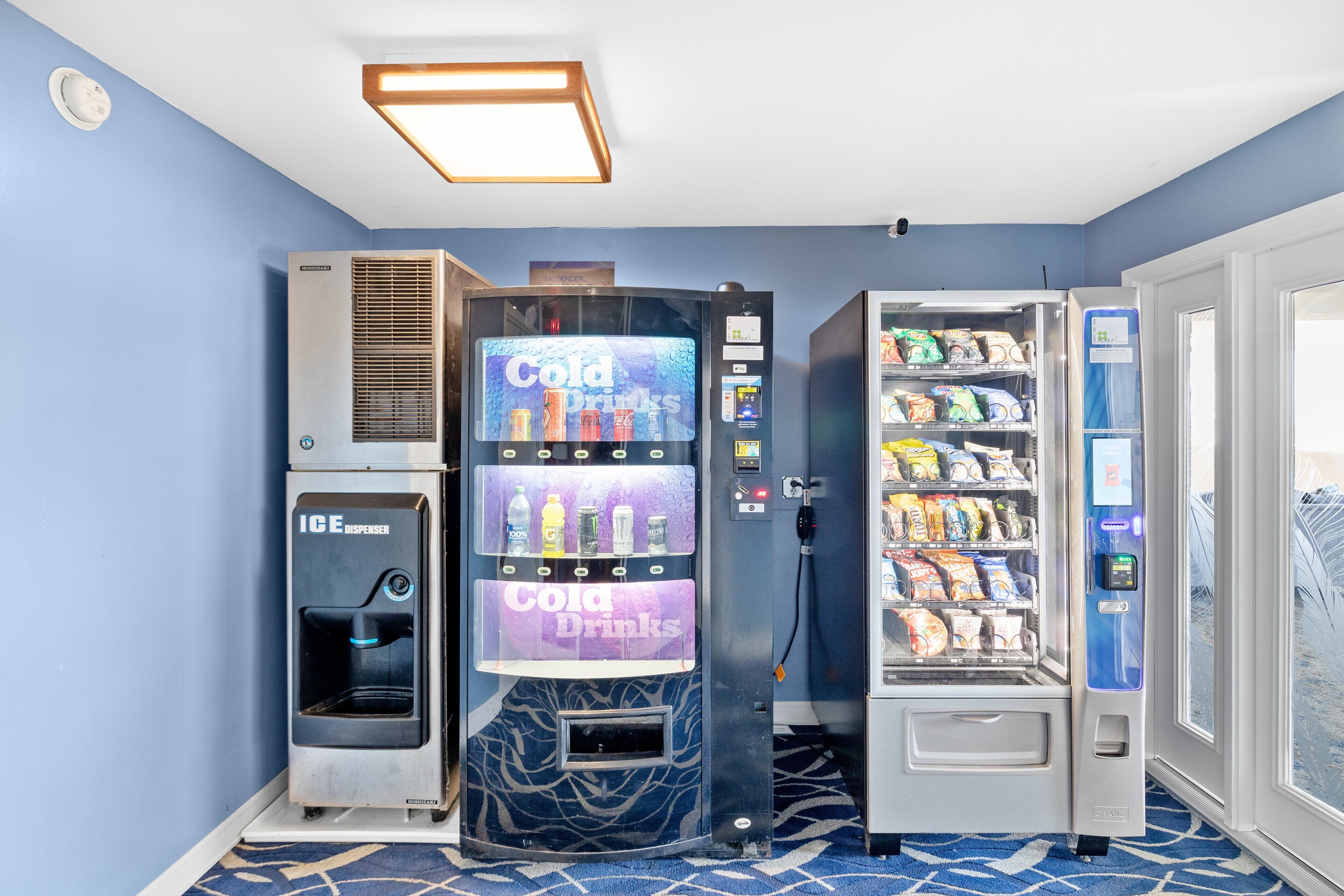 A vending machine area with a beverage dispenser, a vending machine with snacks, and a vending machine with a drink selection.