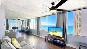 A modern living room with a large TV, grey sofa, and a ceiling fan.