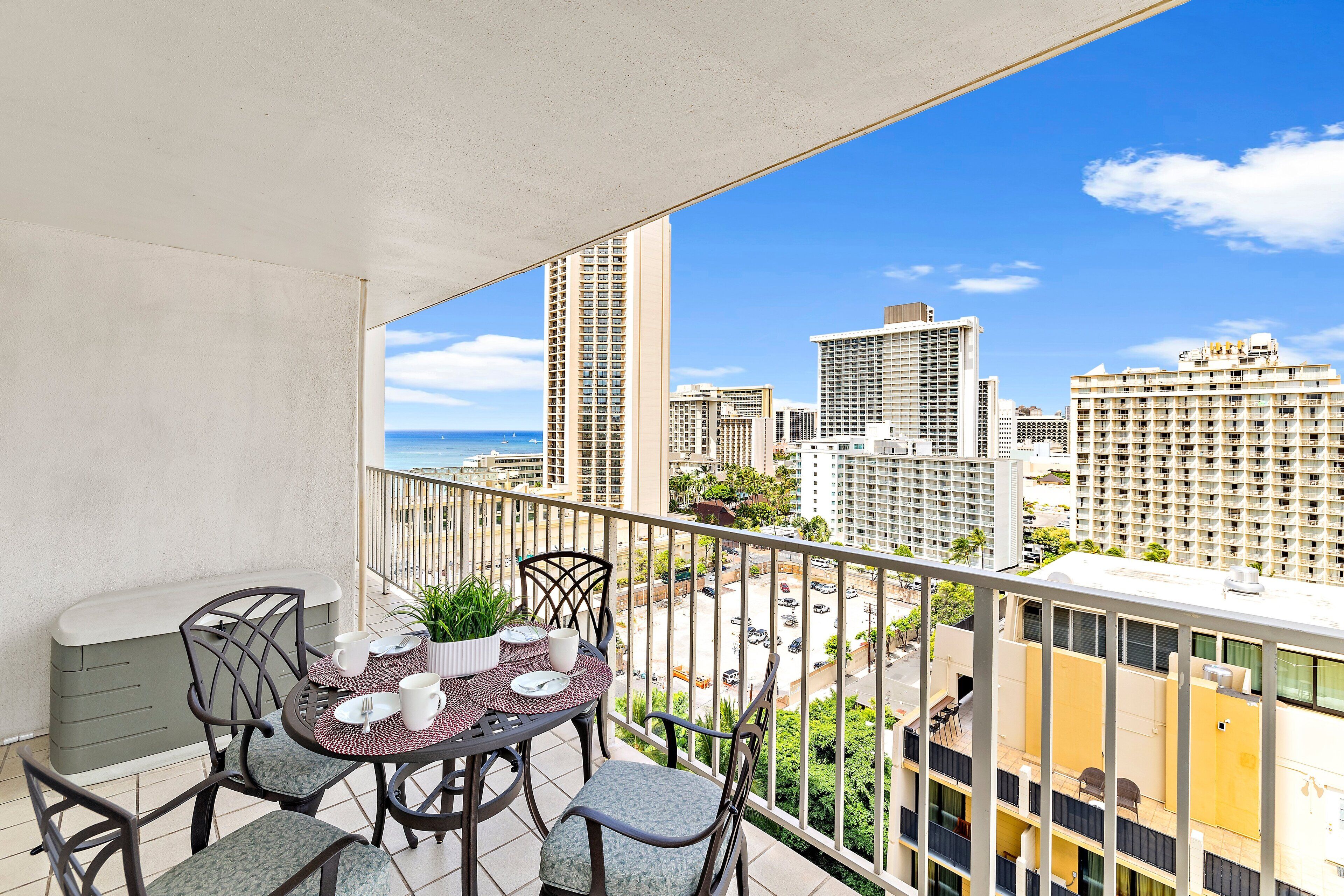 A balcony with a table set for dining, overlooking a cityscape with high-rise buildings and a view of the ocean.