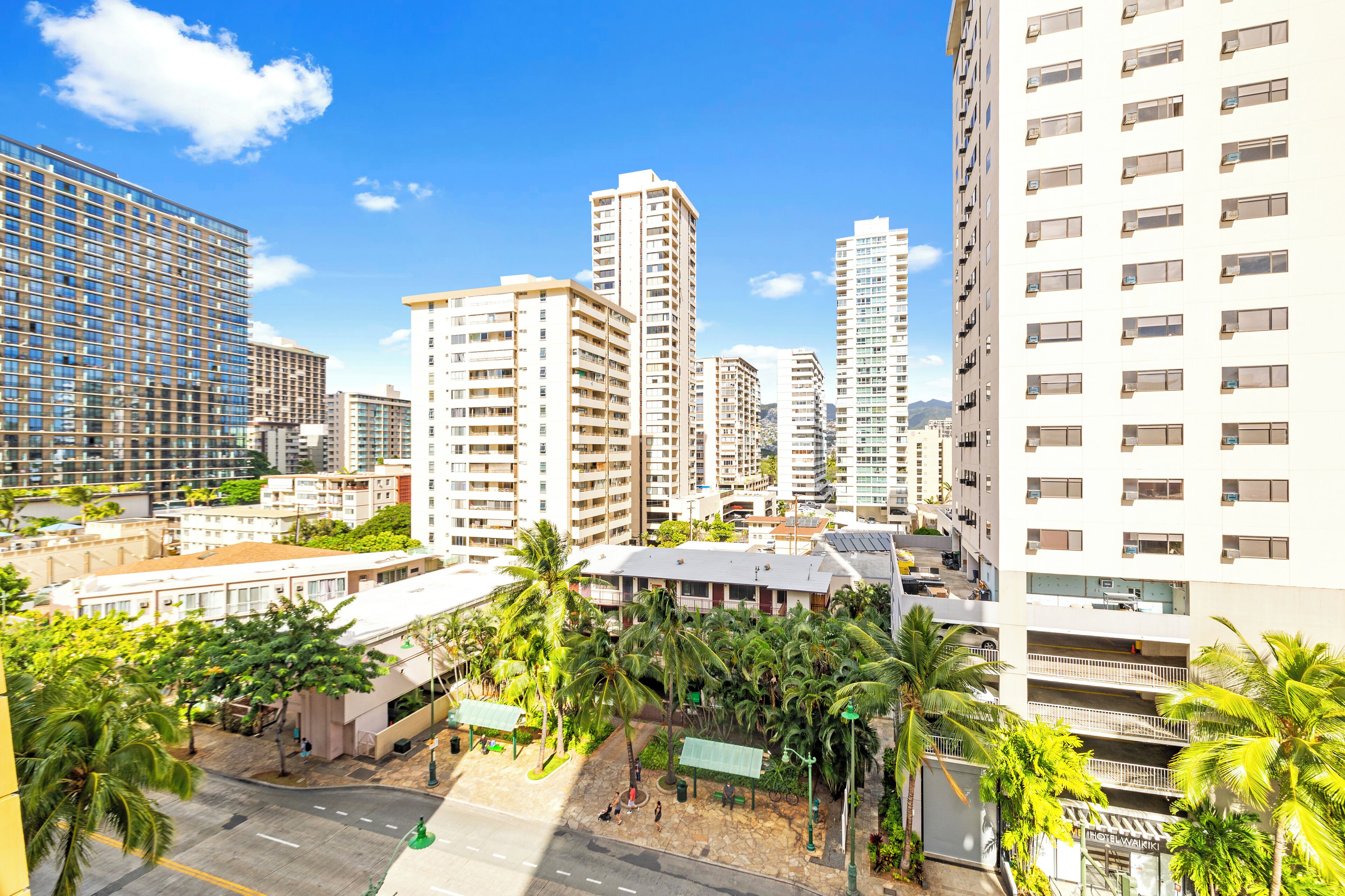 A high-rise hotel with multiple floors, a rooftop terrace, and surrounding palm trees.