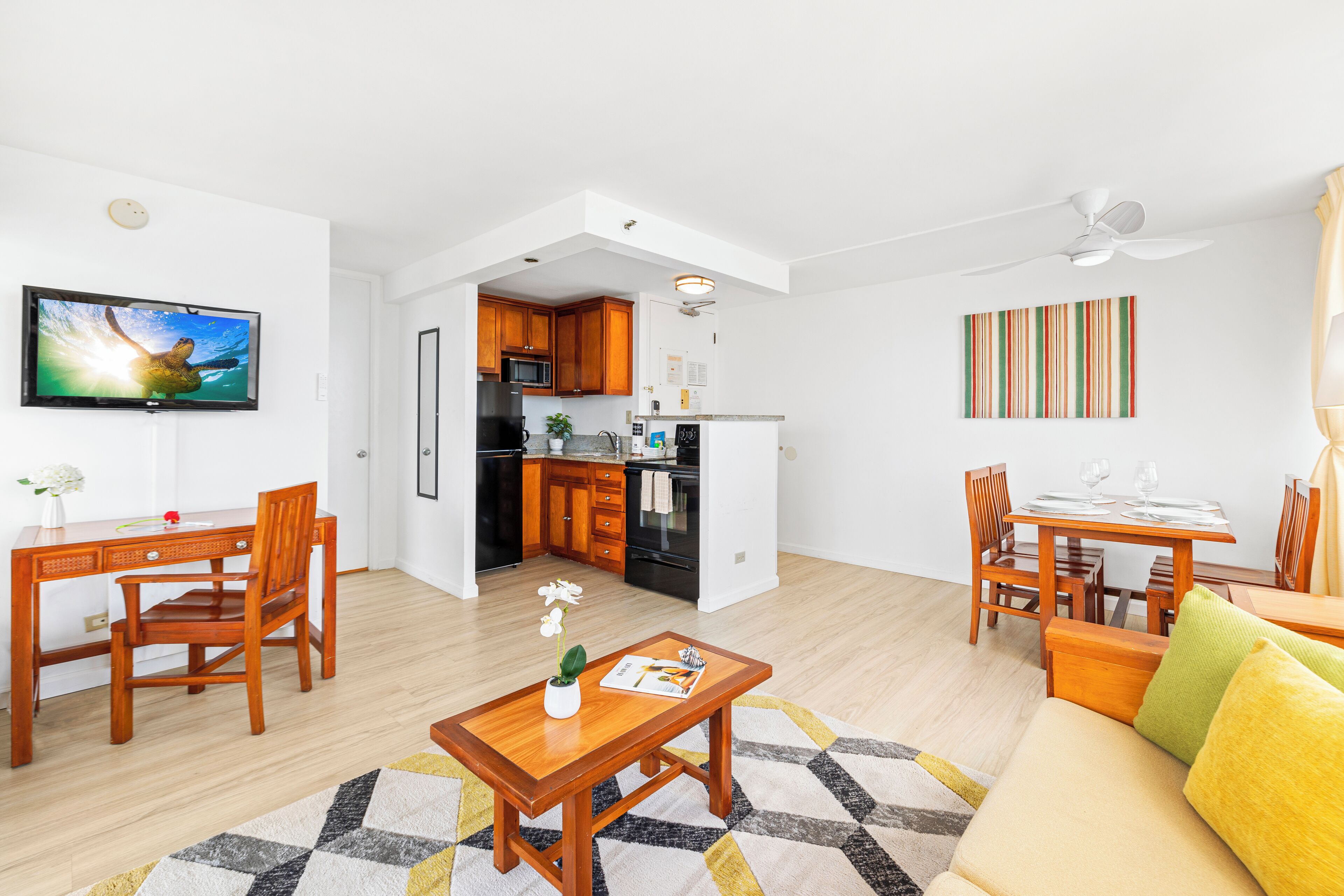 A modern living room with a dining area, kitchen, and a TV mounted on the wall.