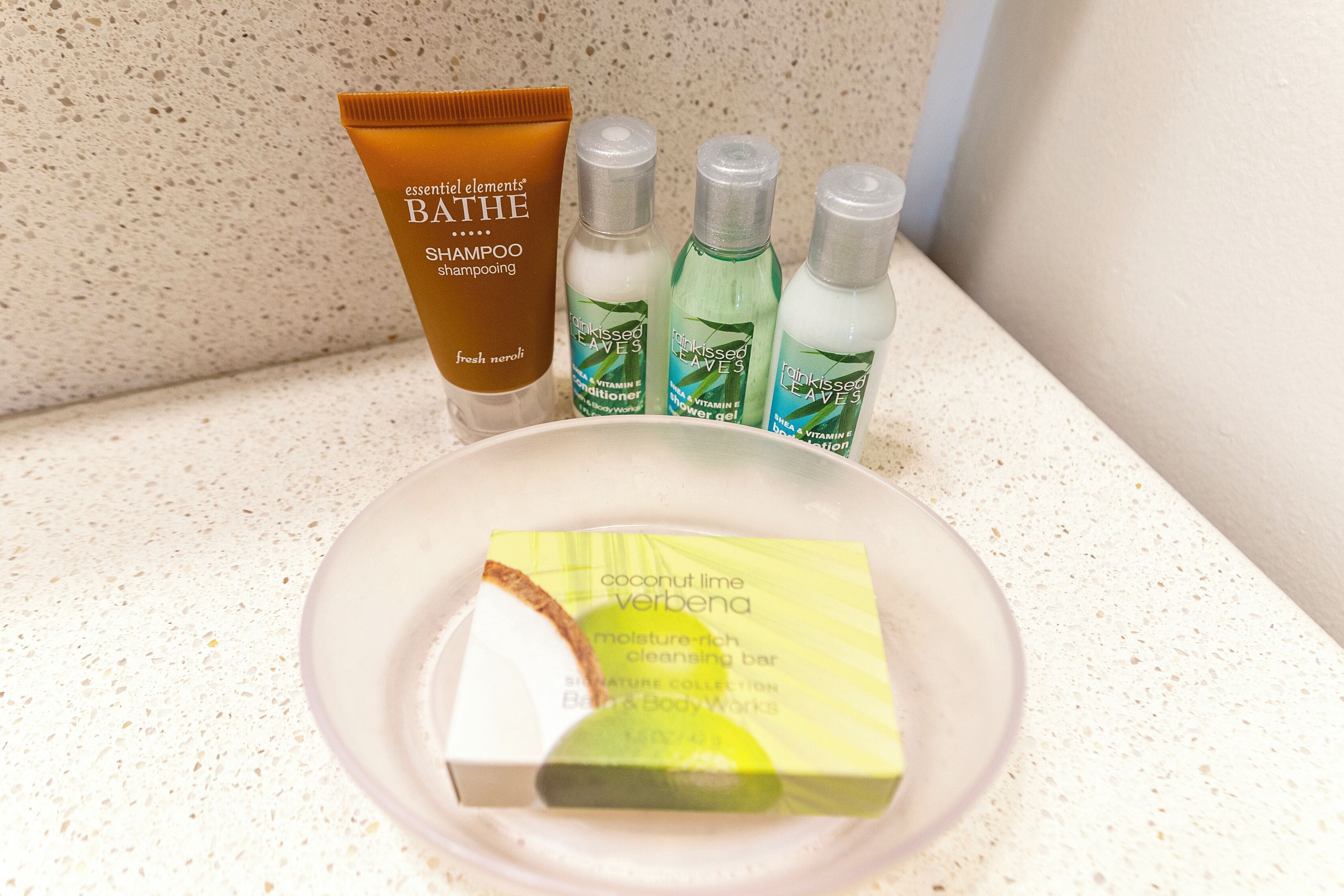 Una encimera de baño con una botella de champú, dos botellas de gel de ducha y una pastilla de jabón.