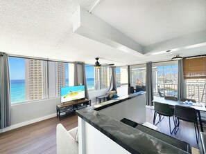 A modern hotel room with a large window offering a view of the ocean and city skyline.