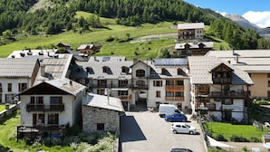 Un grupo de edificios tradicionales de estilo chalet, con fachadas de piedra y balcones de madera, frente a colinas verdes y un cielo despejado.