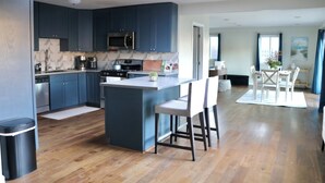 Een moderne keuken met donkerblauwe kastjes, een centraal eiland en een eetgedeelte met witte stoelen en een tafel.