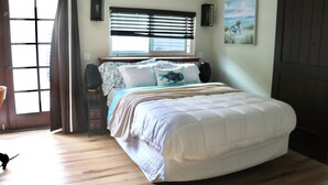 Een slaapkamer met een groot bed, een raam met zonwering, een deur met gordijnen en een schilderij aan de muur.