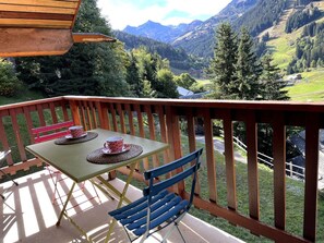 A wooden deck with a table and chairs, overlooking a mountainous landscape. - Appt 8p, ski-in, ski-out, parking (Les Allues)
