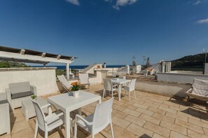 Una terraza en la azotea con mobiliario de mimbre blanco, una pérgola y vistas al mar.