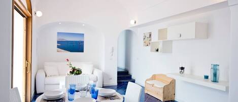 Un comedor moderno con una mesa redonda preparada para cuatro personas, muebles blancos y vista al mar a través de un amplio ventanal.