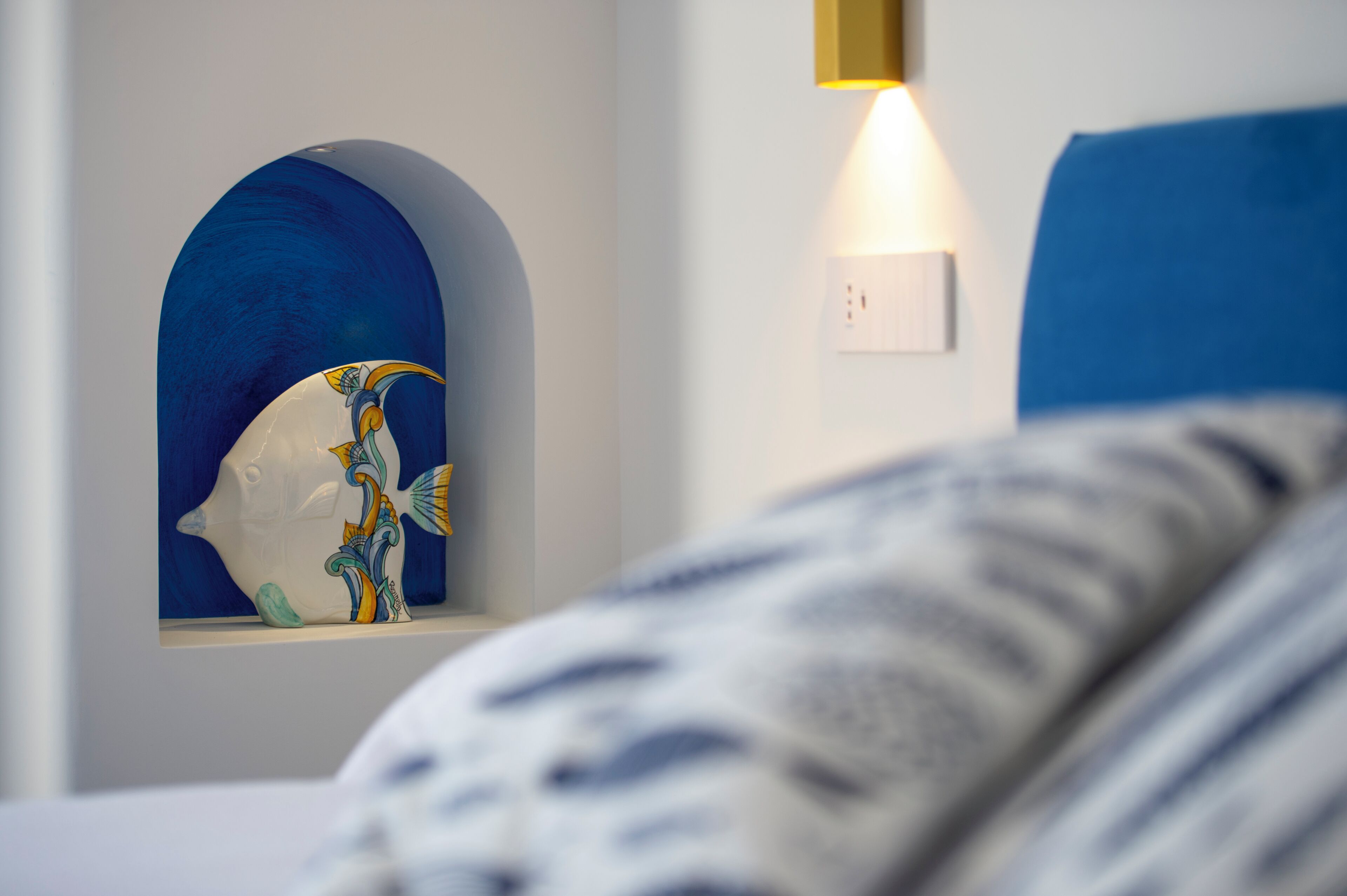 A bedroom with a bed, a wall-mounted shelf with a decorative fish sculpture, and a wall-mounted light fixture.