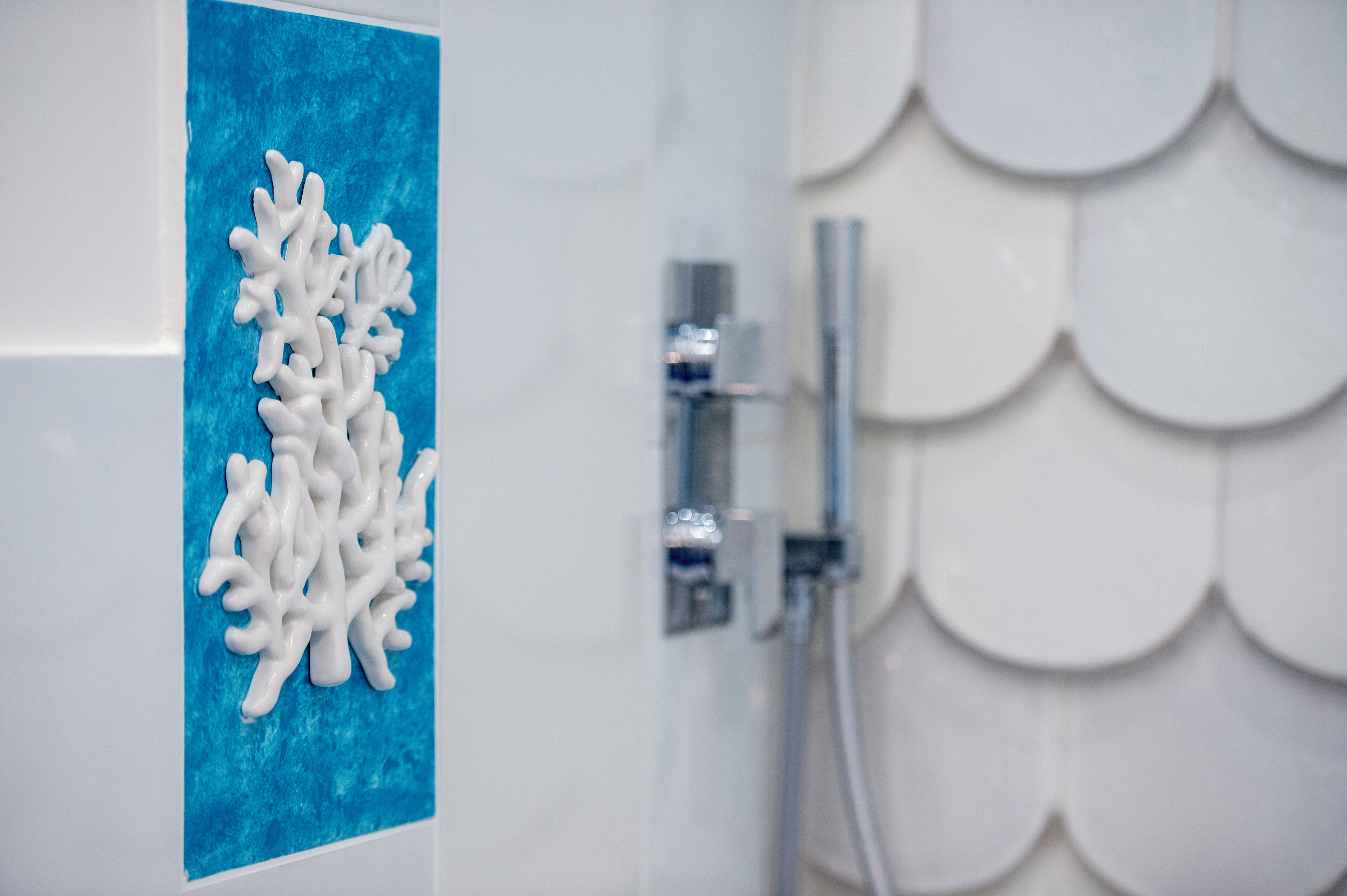 A bathroom with a blue accent wall, a white coral-like decoration, and a shower with a scalloped tile design.
