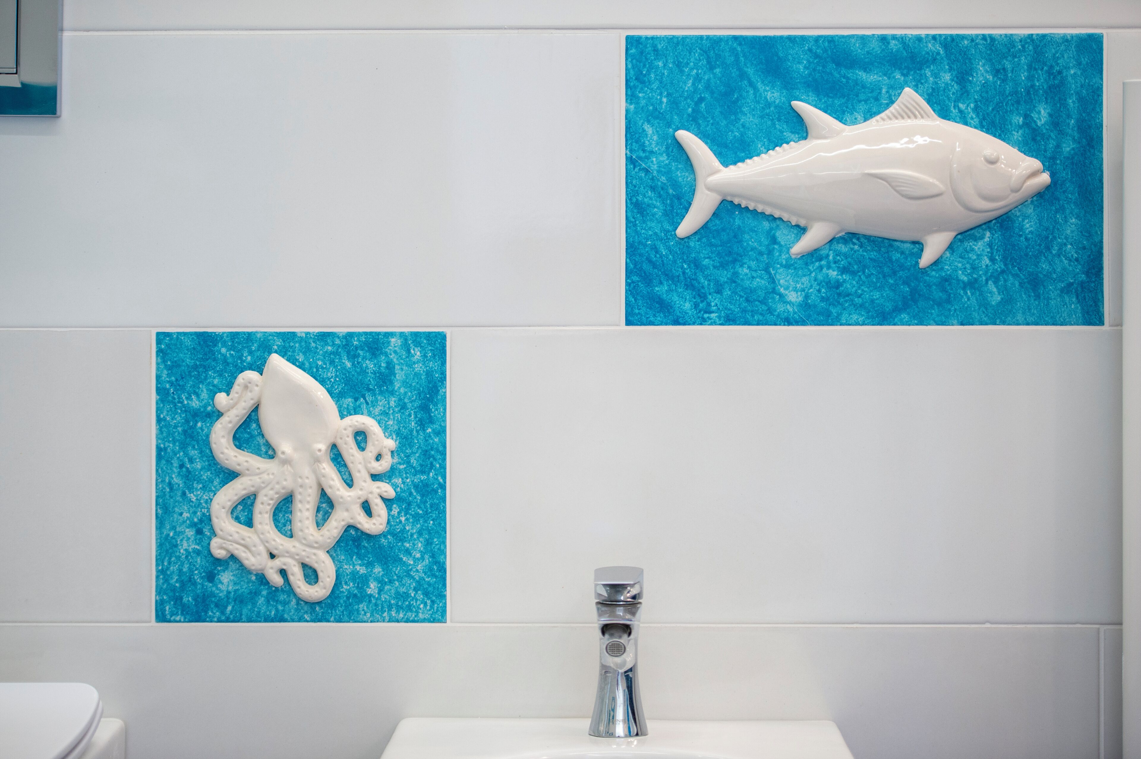 Un baño con un lavamanos blanco, un inodoro blanco y dos adornos de peces colgados en la pared.
