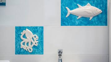 Un baño con un lavamanos blanco, un inodoro blanco y dos adornos de peces colgados en la pared.