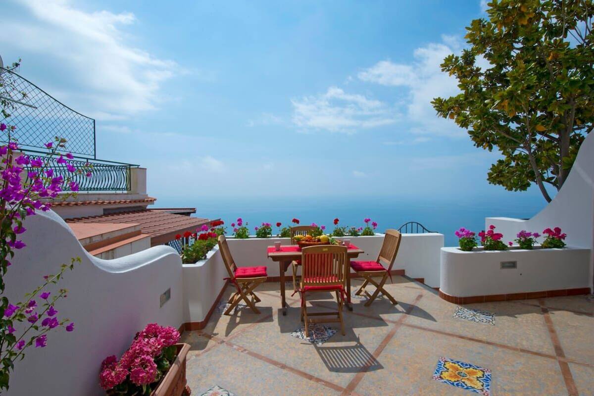 Une terrasse avec une table et des chaises, une vue sur la mer et des plantes en pot.