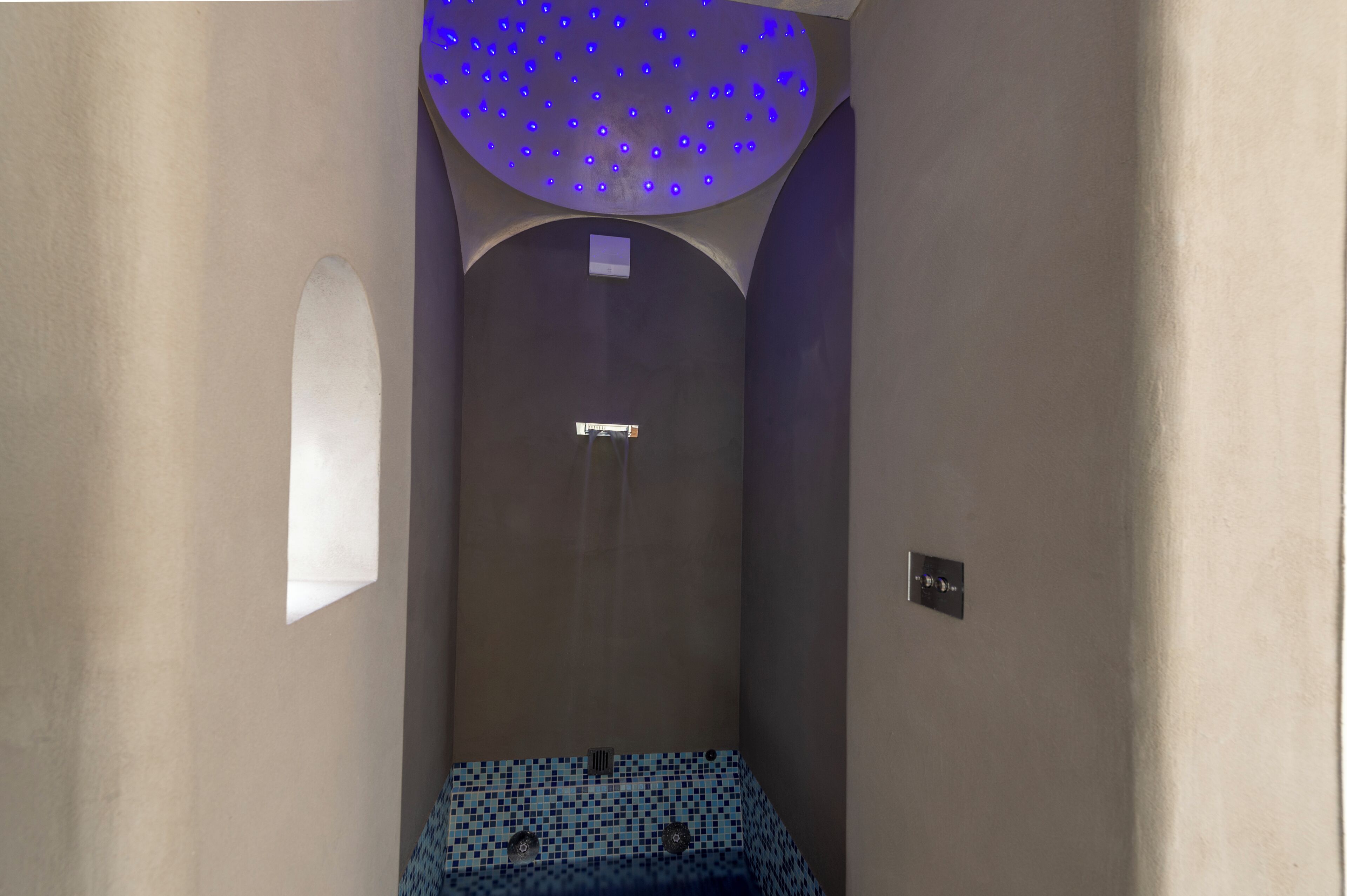 Een smalle, afgesloten ruimte met een betegelde vloer en een plafond met blauwe verlichting.