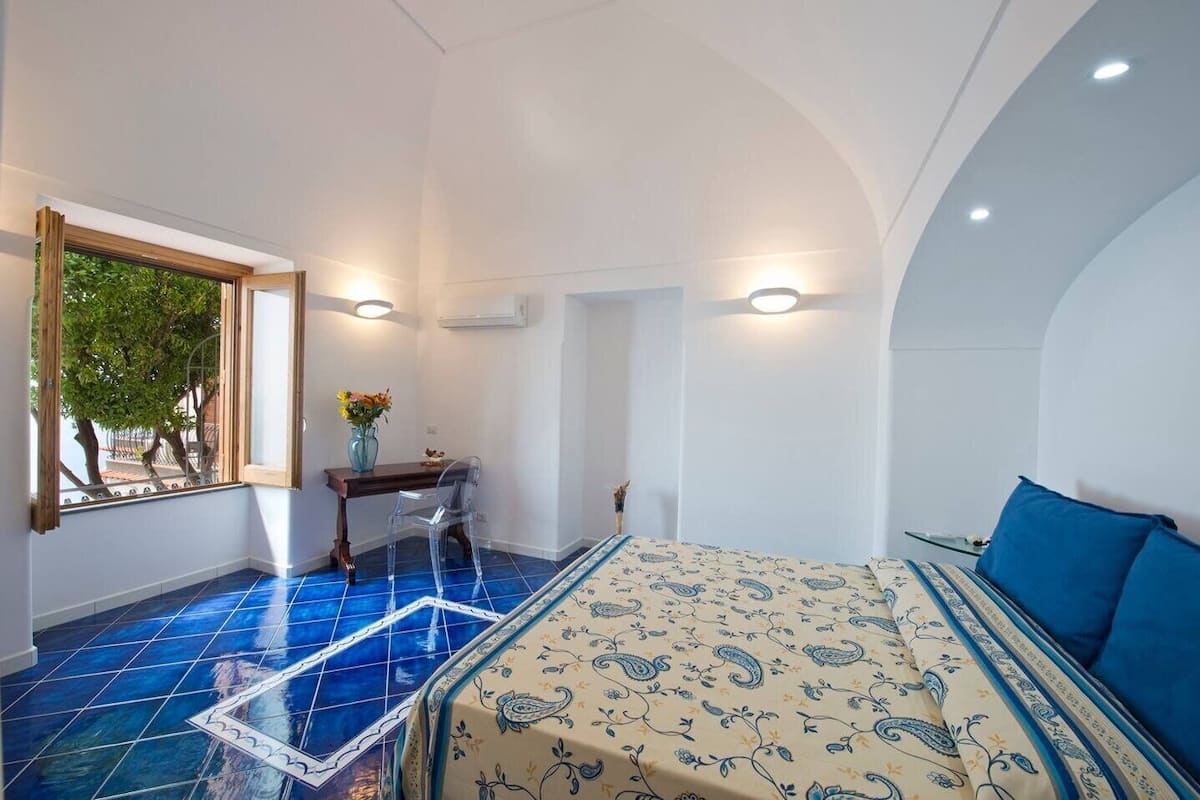 Une chambre à coucher avec un lit, un bureau et une chaise. Il y a une fenêtre qui donne sur des arbres.