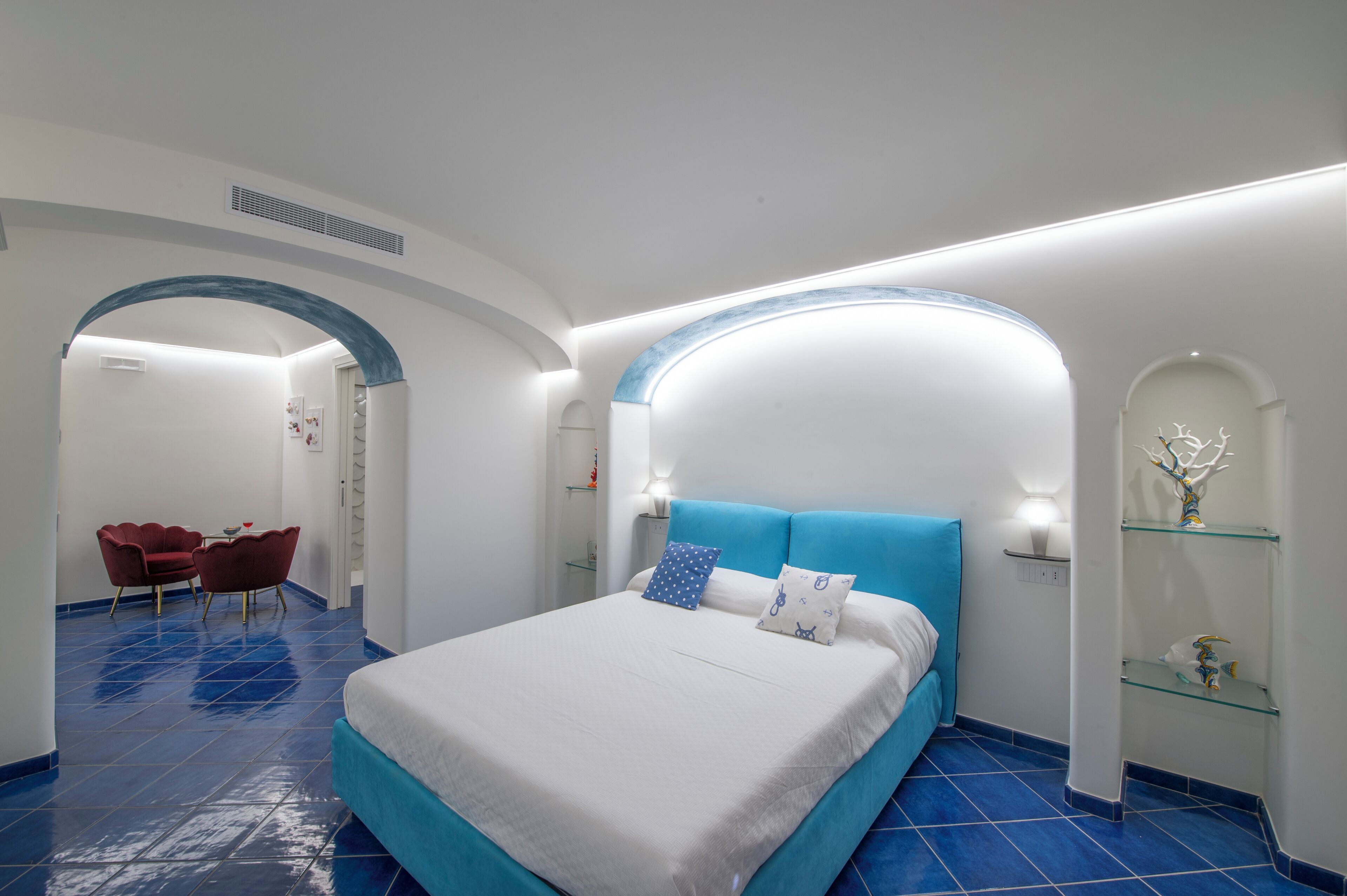Een moderne hotelkamer met een groot bed, een bureau met twee stoelen en een glazen plank met decoratieve objecten.