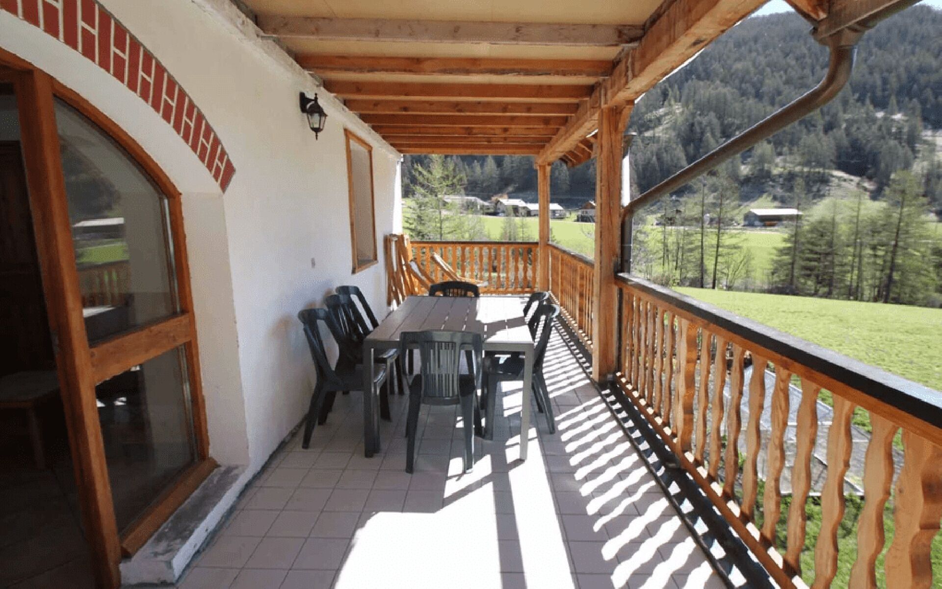 A covered outdoor patio with a wooden table and chairs, a view of a green landscape, and a mountain in the background.