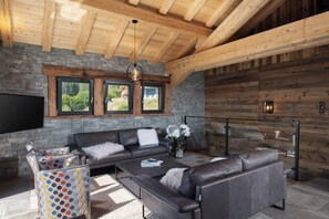A modern living room with a stone wall, wooden beams, a large flat-screen TV, leather sofas, and a coffee table. - L'Edelweiss - Luxury chalet with Jacuzzi & Sauna, Gérardmer (Gérardmer)