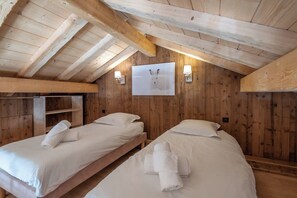 A room with two beds, wooden walls, and a ceiling with exposed beams.