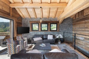 A modern living room with a stone fireplace, leather sofas, and a large TV.
