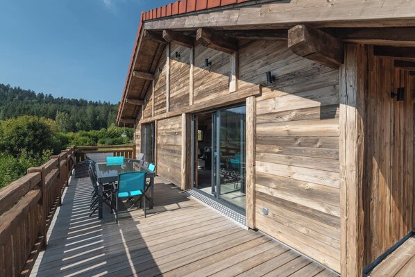 A wooden cabin with a deck, glass sliding doors, and a view of the forest.