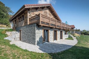 A modern two-story house with a stone facade, wooden balcony, and a stone pathway leading to the entrance.
