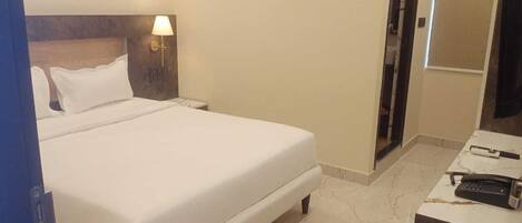 Habitación de hotel con cama, mesita de noche con lámpara, escritorio con teléfono y puerta que da a otra habitación.