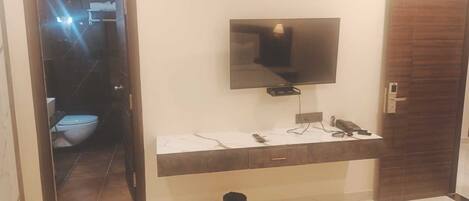 A bathroom with a toilet, a sink, a mirror, and a television mounted above the sink.