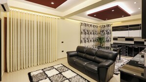 A modern living room with a black leather sofa, a patterned rug, and a kitchen area with black and white cabinetry. - Hotel Mimani (Berat)