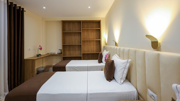Ein Hotelzimmer mit zwei Betten, einem Holzkopfteil, einem kleinen Schreibtisch und einer eingebauten Regaleinheit.