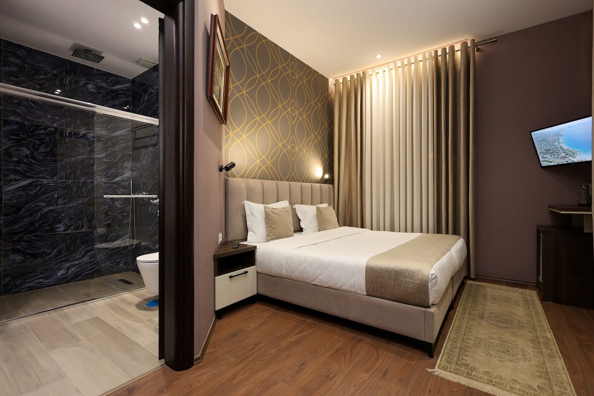 Quarto de hotel moderno com uma cama grande, área de chuveiro e televisão.