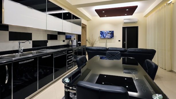 A modern kitchen with black and white cabinetry, a glass dining table, and black leather sofas. - Hotel Mimani (Berat)