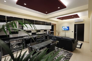 Una cocina moderna con armarios blancos y negros, una zona de comedor con mesa de vidrio y un sofá de cuero negro.