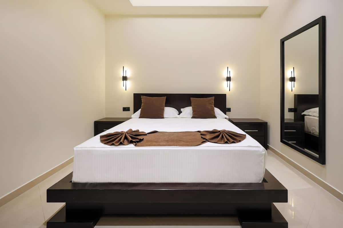 Quarto de hotel moderno com uma cama grande, duas mesas de cabeceira e um espelho grande na parede.