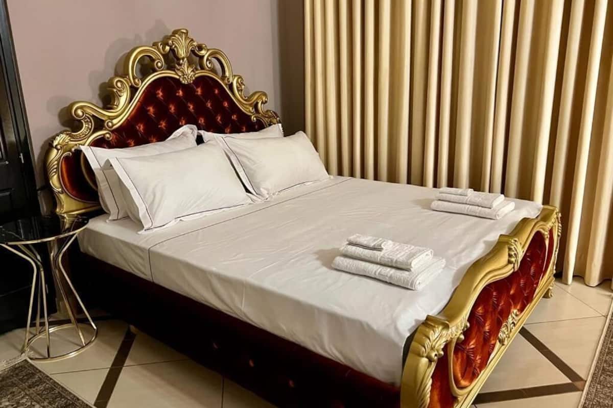 Uma cama com estrutura dourada e estofamento vermelho, roupa de cama branca e um par de toalhas dobradas sobre a cama.