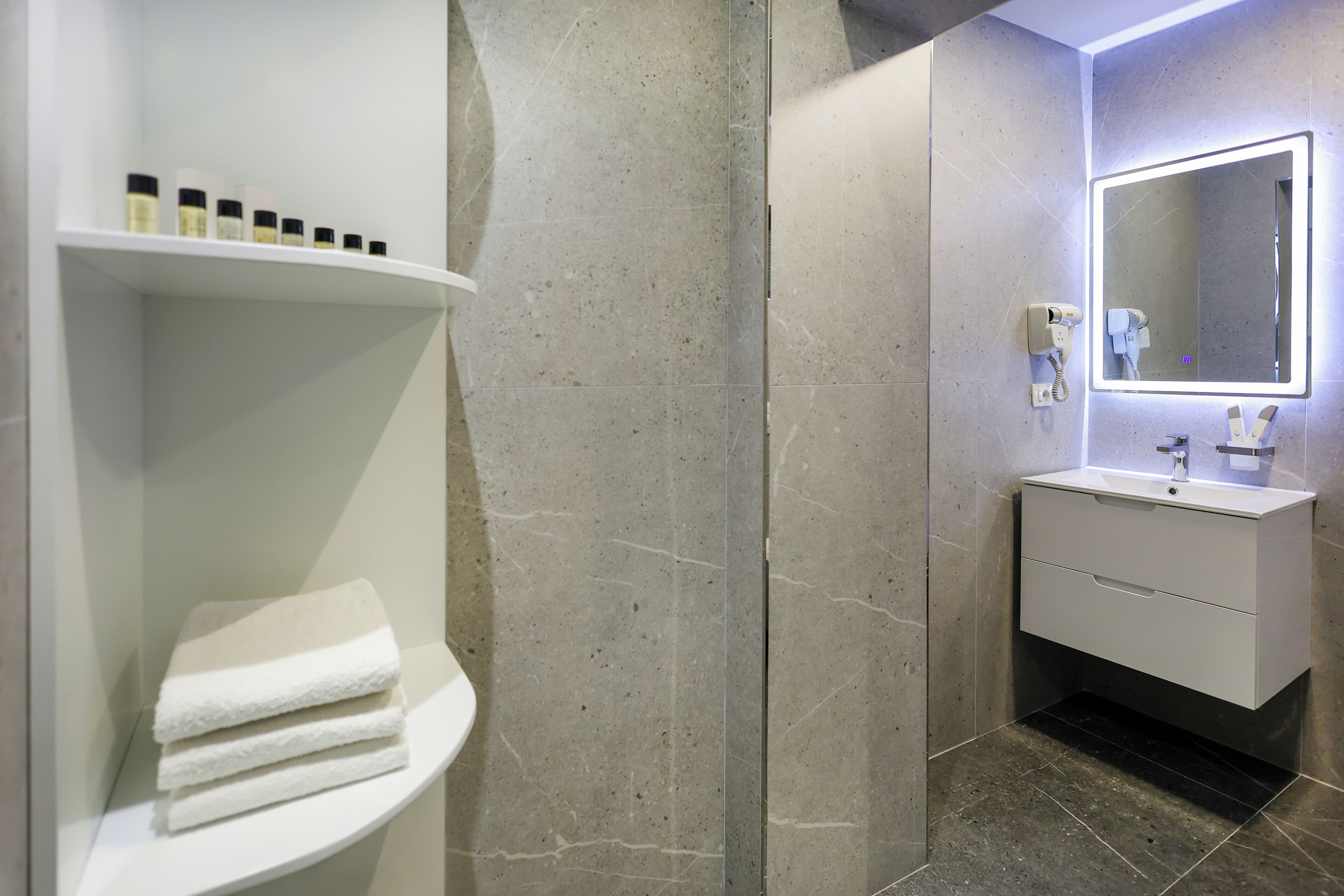 A modern bathroom with a white vanity, a large mirror, and a shelf with toiletries.